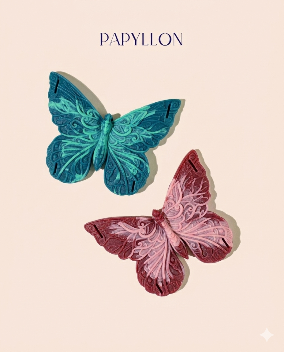 Deux papyllons en silicone effet marbré, le premier est bleu canard avec des marbrures vert turquoise, et le seconde rouge bordeaux avec des marbrures roses poudrés. une inscription Papyllon est visible en haut de l'image. Les deux objets intimes en silicones sont posés sur un fond beige