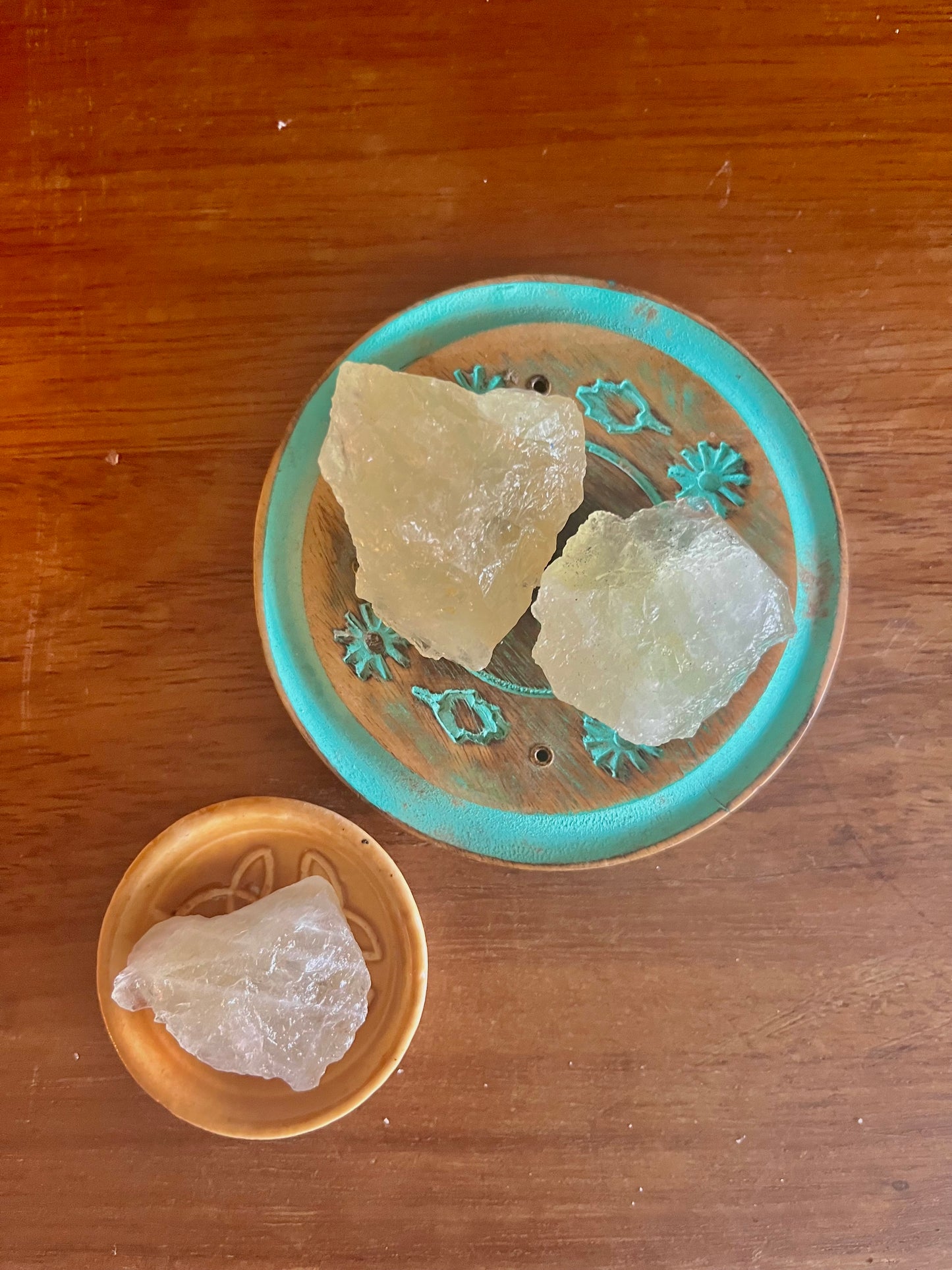 Pierre demi précieuse Citrine brute. inclus dans les bougies Krystal de la marque Playsir dans le collection Découverte et curiosité. Pierres naturelles Jaunes translucides, posé dans une petite coupelle en terre cuite et une autre en bois peint sur une surface en bois massif. Vue de dessus