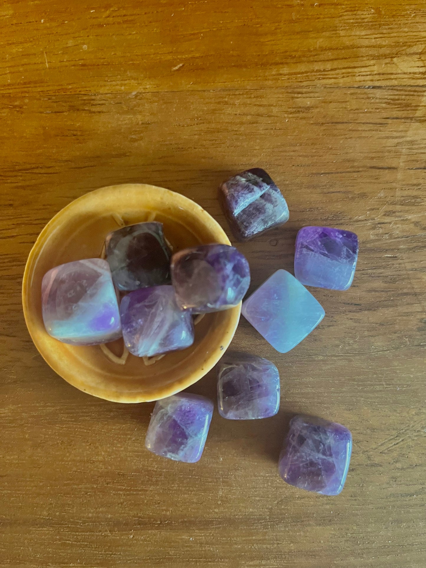 Plusieurs pierres Améthyste taillés en cubes et polie posé dans une coupelle en terre cuite sur une surface en bois massif. Ces pierres sont incluses dans les Bougies Krystal de la marque Playsir.