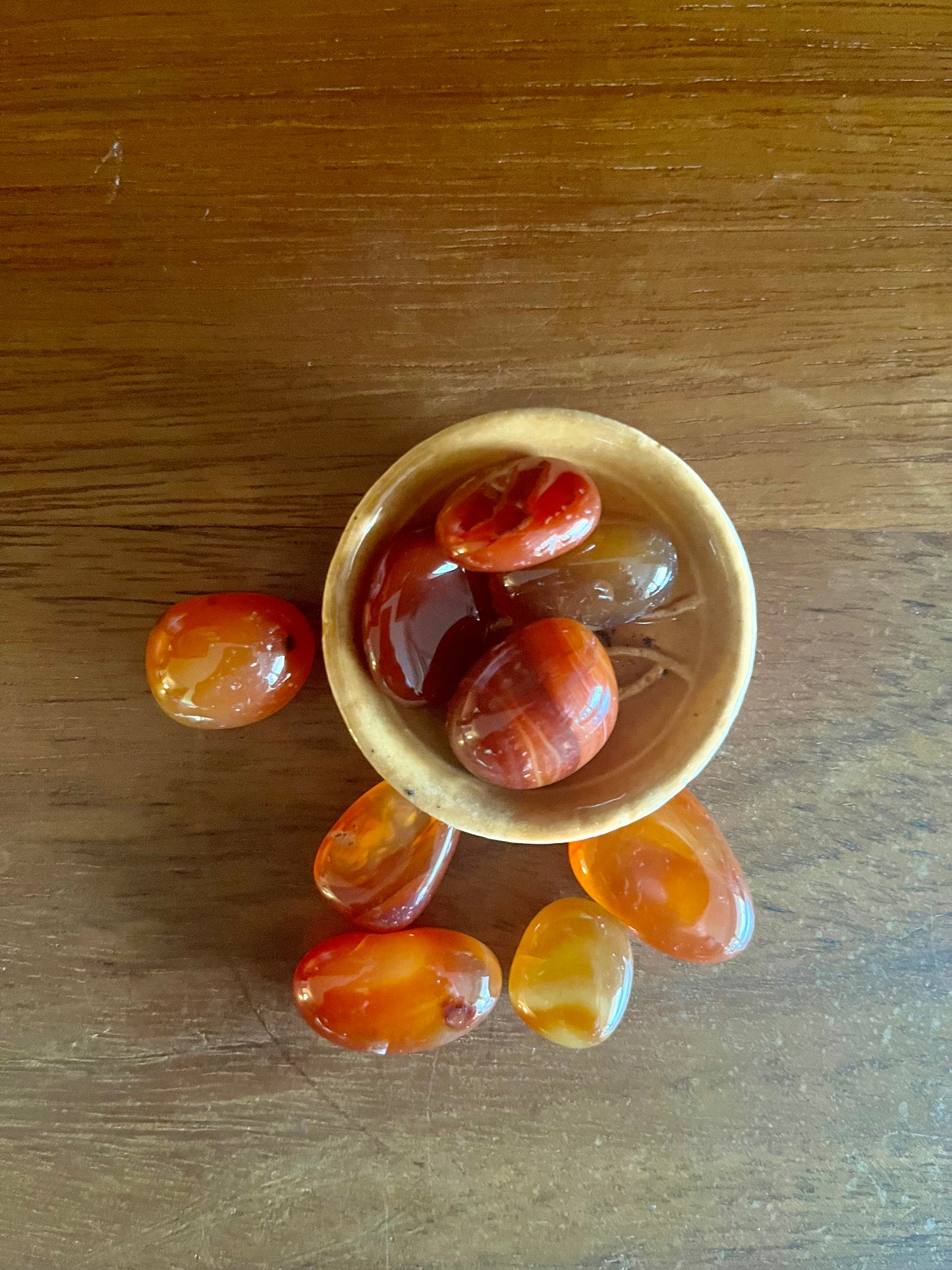 Pierres polies Cornaline, inclus dans les bougies Krystal de la marque playsir. accessoire intime et de bien-être. Vue d'au dessus, les pierres cornalines sont posé sur une surface en bois, quatres pierres sont dans une petites coupelle en terre cuite.